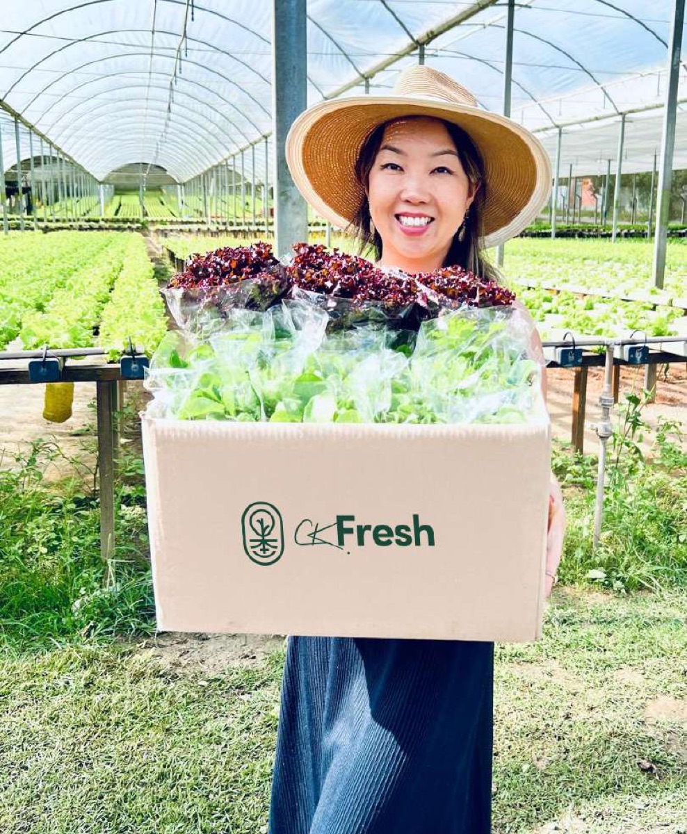 Camila Kuramoto segurando uma caixa de hortaliças CK Fresh na estufa